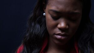 woman's face looking sad, eyes down, dark background
